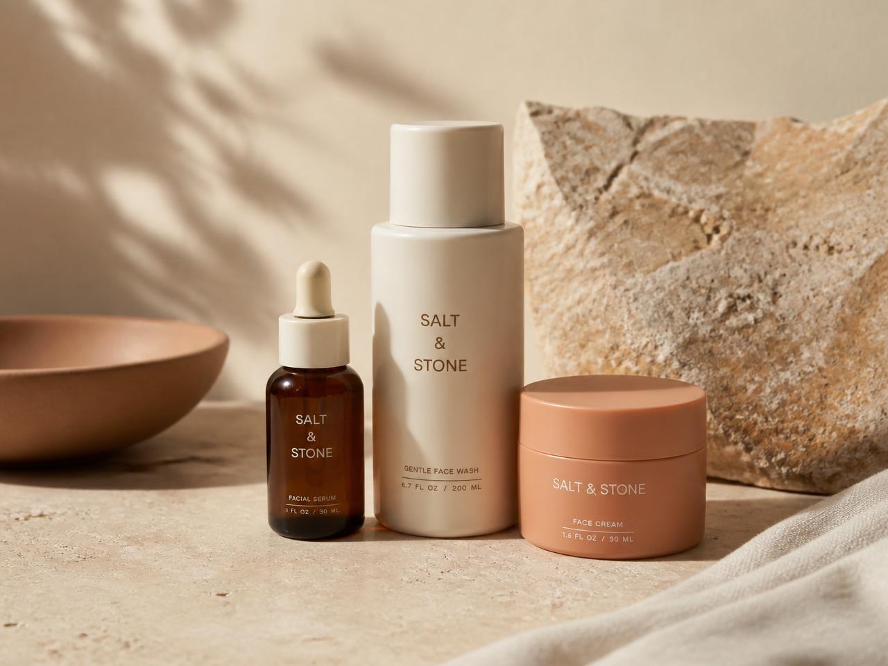 Simple skincare bottles and a serum dropper on a warm stone surface
